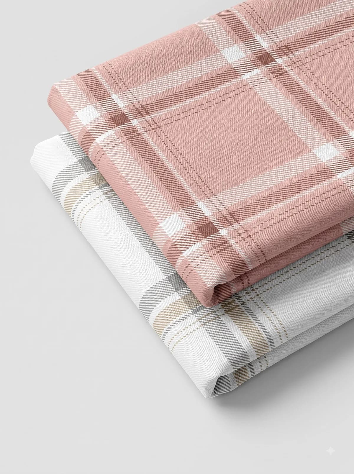 Folded blush pink and grey tartan fabrics stacked on a pale grey background