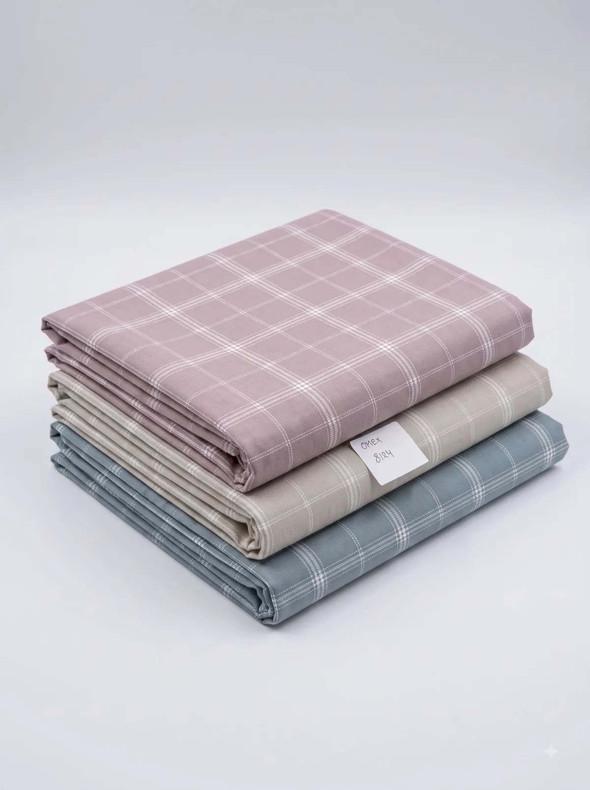 Folded dusty rose, beige and slate blue windowpane check fabrics stacked on a white background