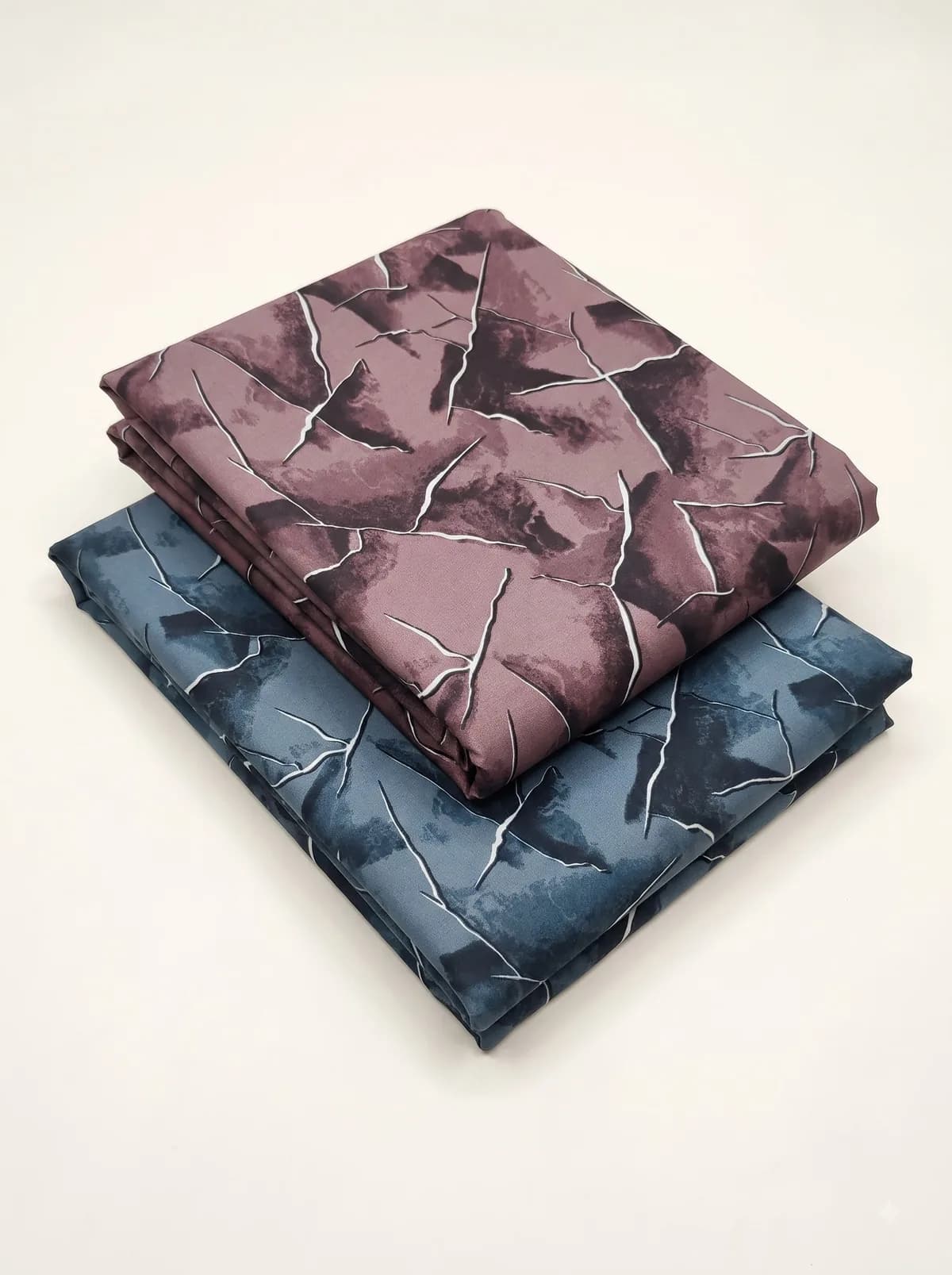 Folded mauve and slate blue fractured marble print fabrics stacked on a cream background