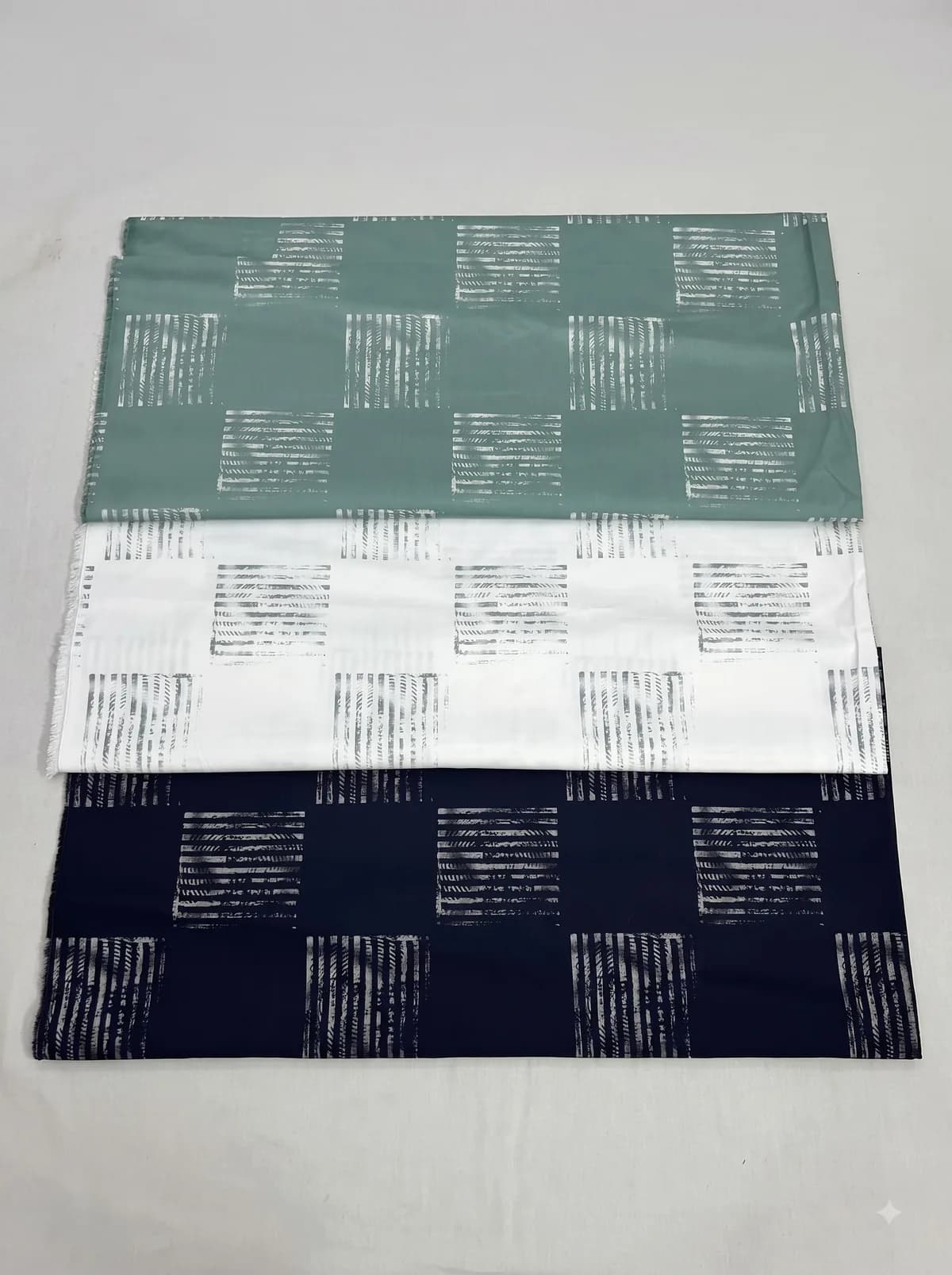 Sage, ivory and navy hatched square print fabrics laid out on a grey background