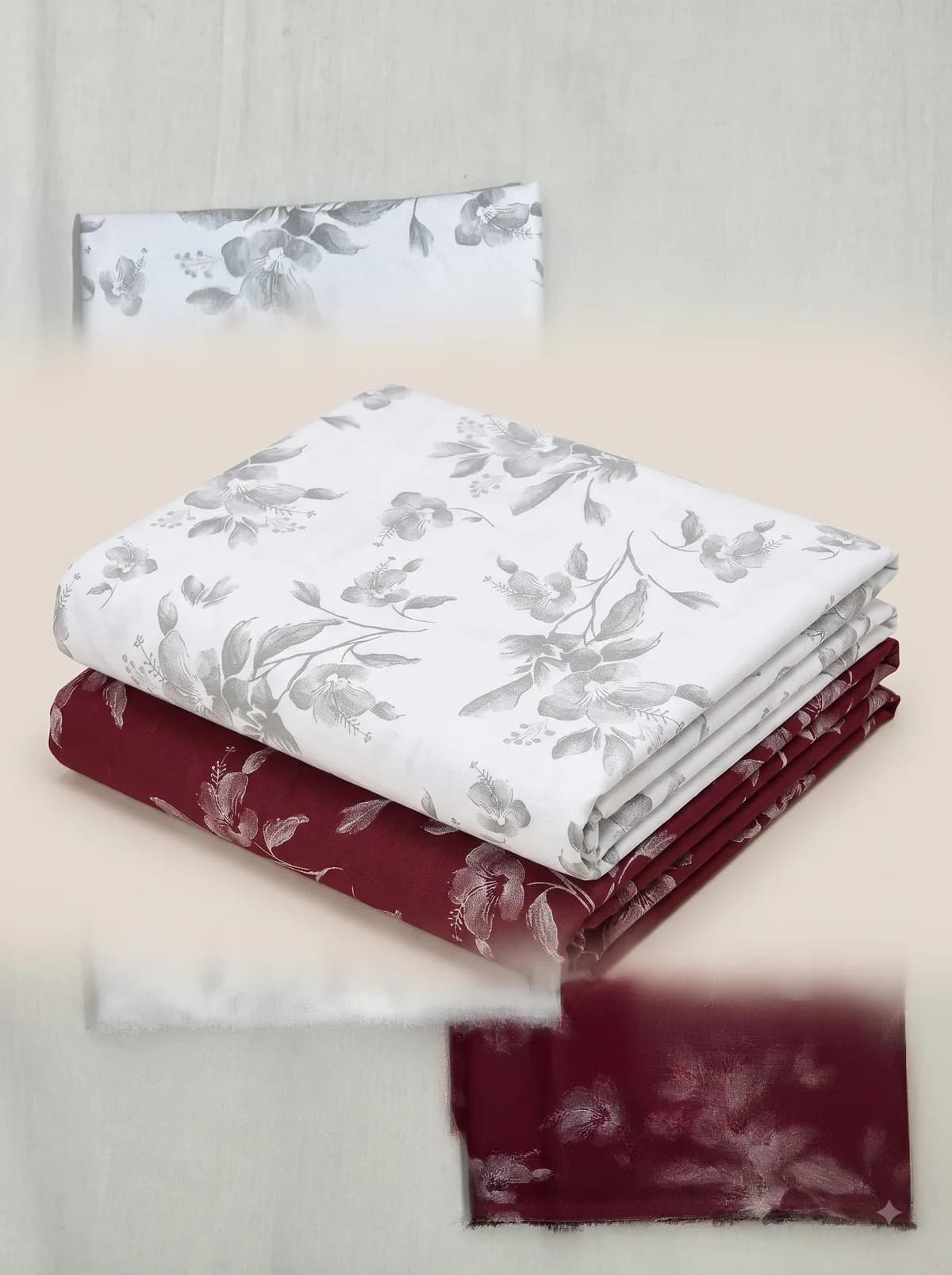 Folded ivory and burgundy grey hibiscus print fabrics stacked on a beige background