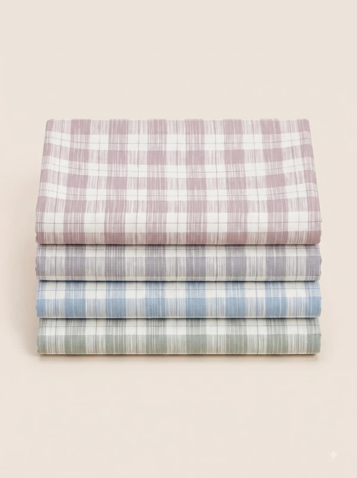 Folded mauve, grey, blue and sage ikat check fabrics stacked on a beige background