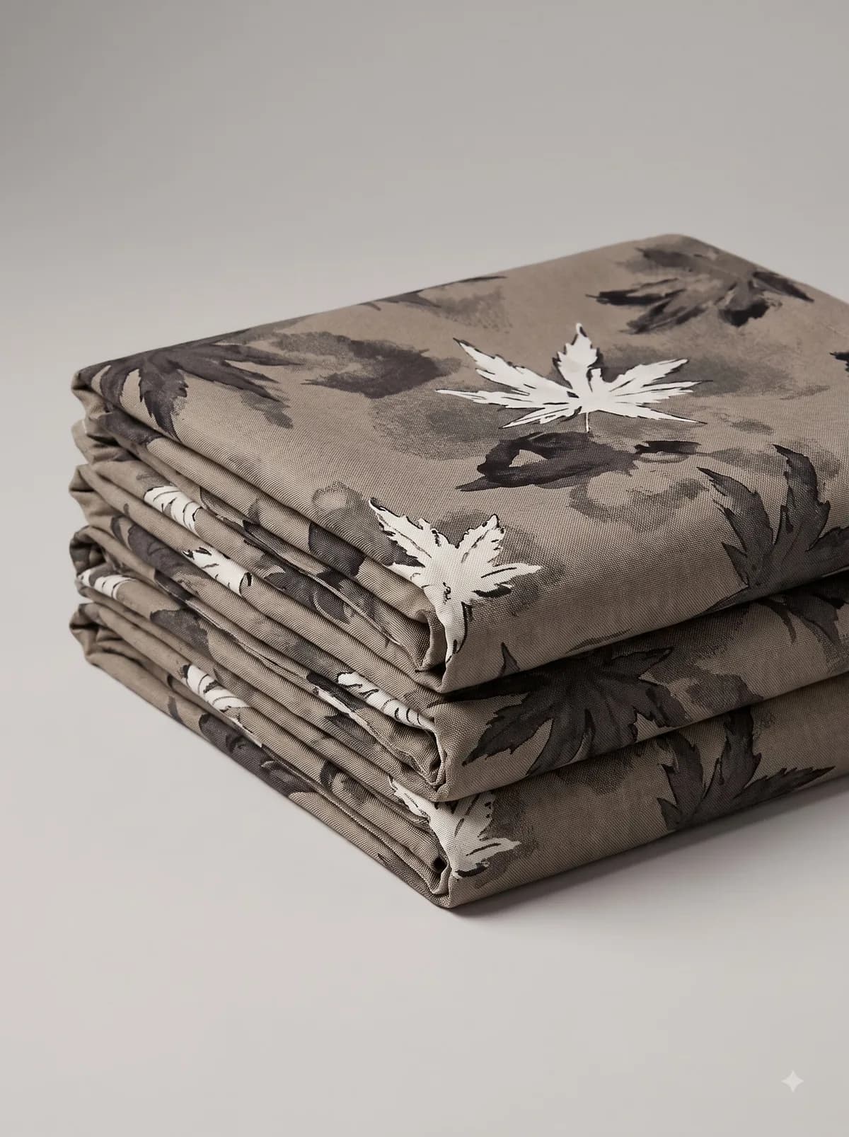 Stack of folded taupe watercolour maple leaf print fabrics on a grey background