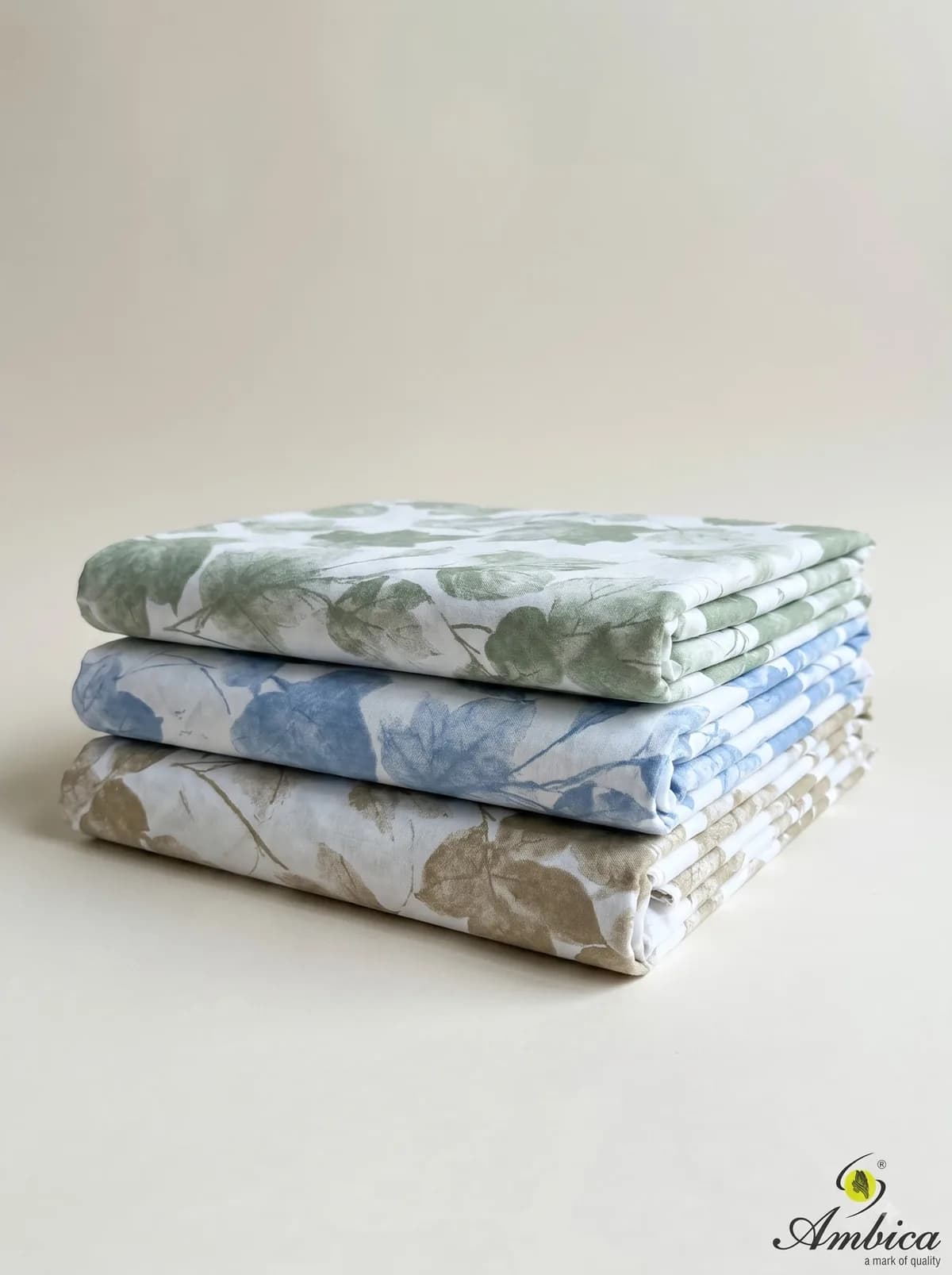 Three folded leaf print fabrics in beige, blue and green on a cream background