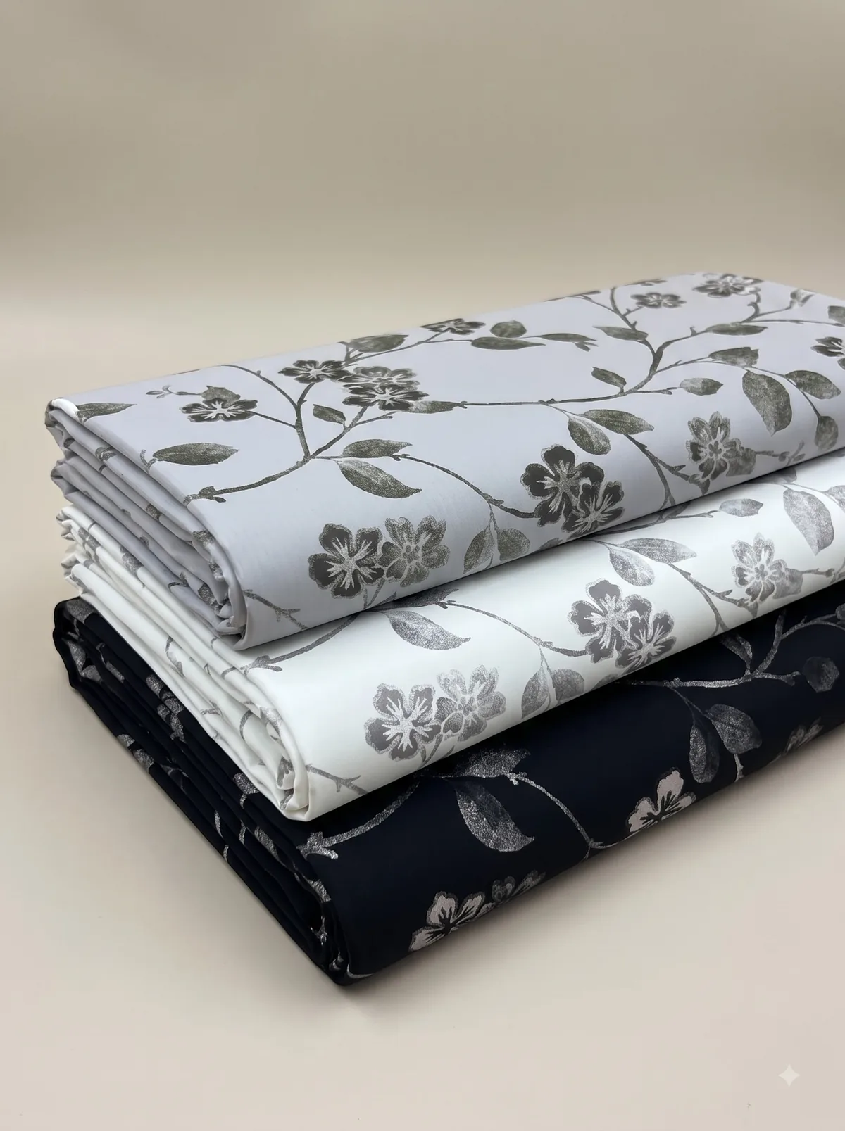Folded mauve, beige and teal watercolour floral fabrics stacked on a grey background