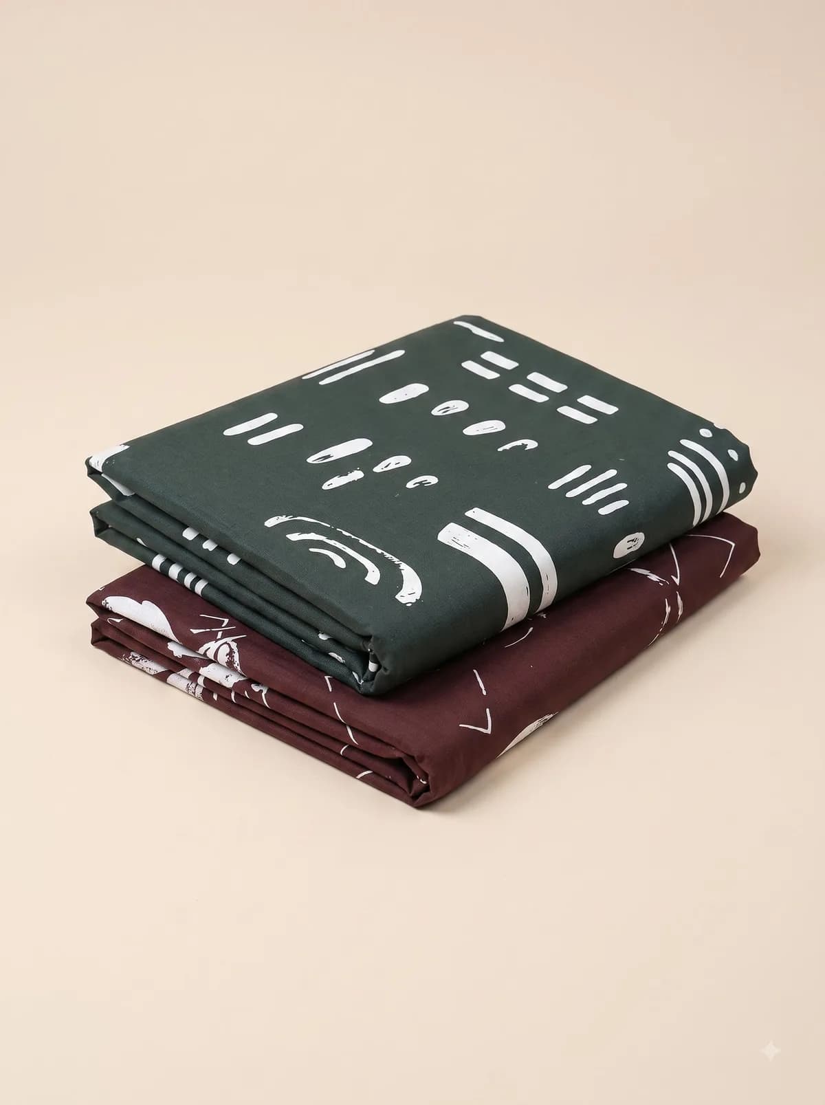 Folded green and maroon mudcloth brush print fabrics stacked on a beige background