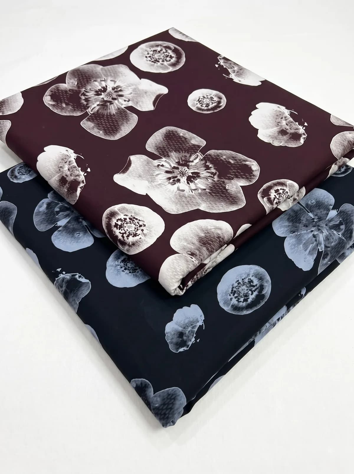 Folded burgundy and navy large poppy print fabrics stacked on a white background