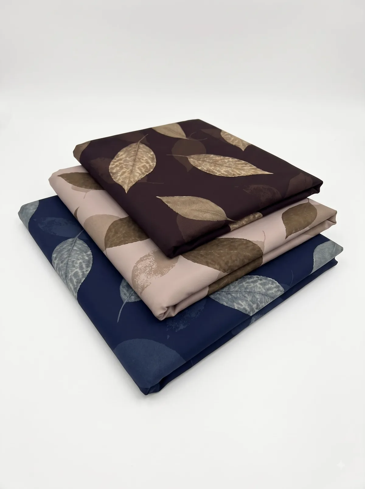 Folded burgundy, beige and navy large veined leaf print fabrics stacked on a white background